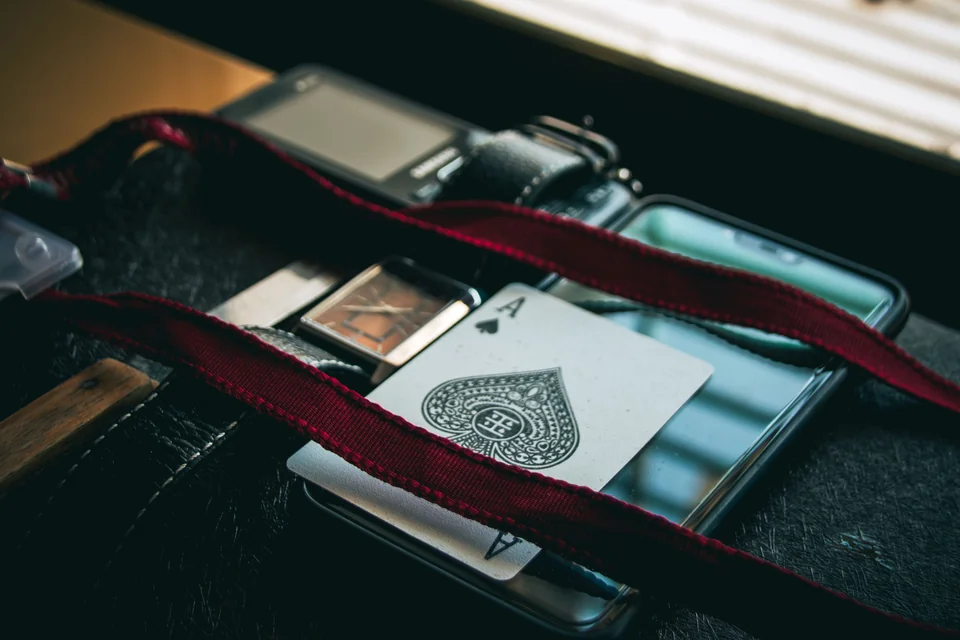 An ace of spades placed on a phone beside a wristwatch.
