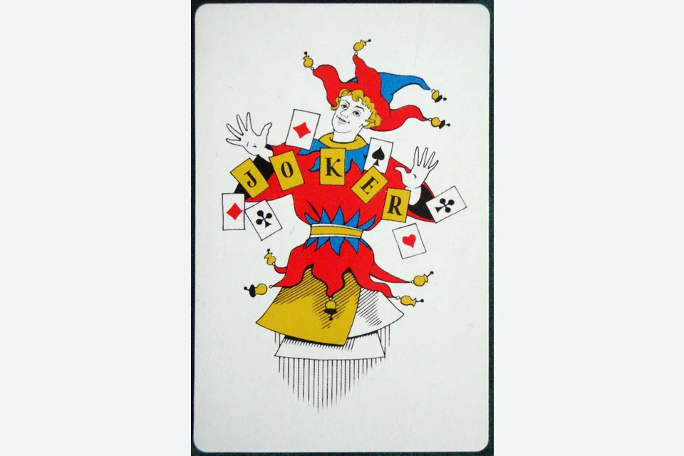 A close-up photograph of a physical Joker card with a red, blue and yellow jester design.