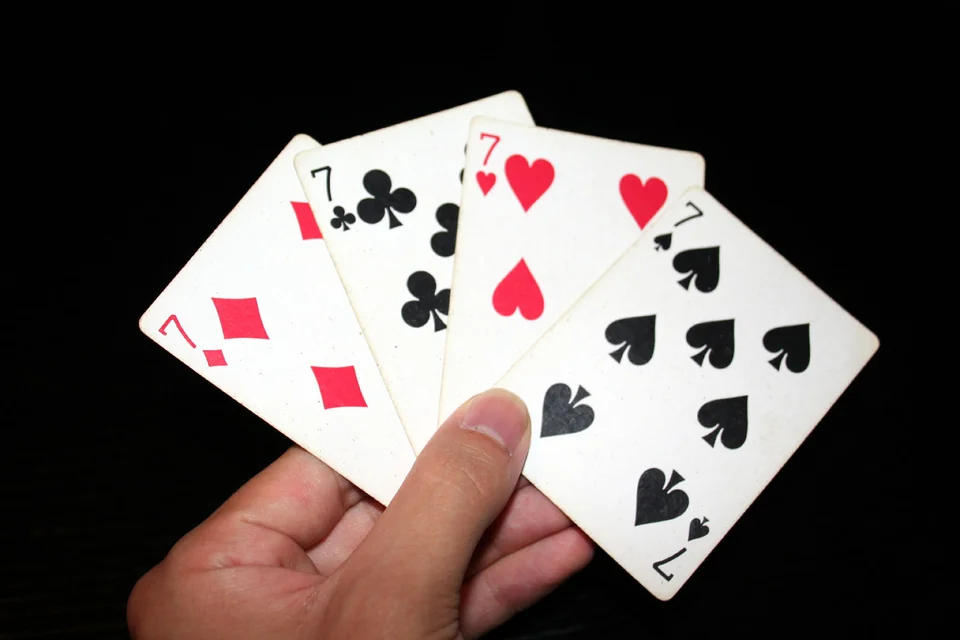 A hand holding the seven of diamonds, clubs, hearts and spades against a dark background.